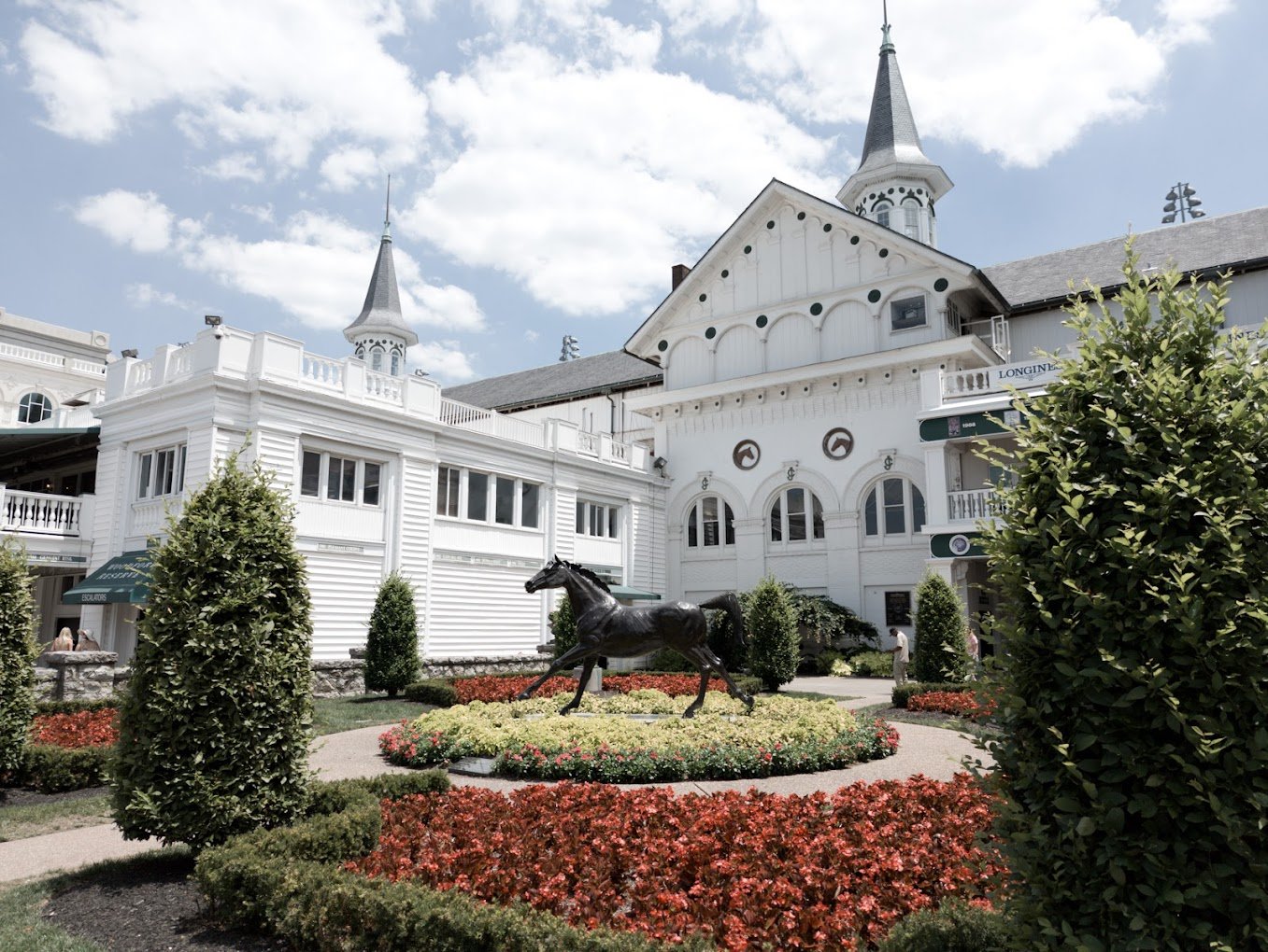 White Churchill Downs buildings with twin spires and a horse statue in a garden courtyard
