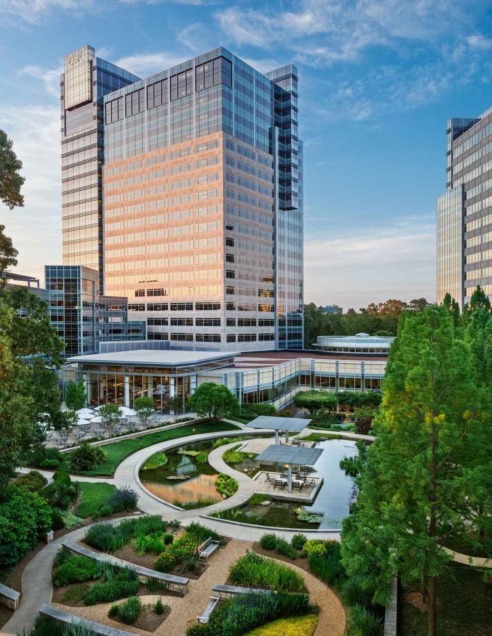 Cox Communications campus towers at sunset above a landscaped courtyard with reflecting ponds