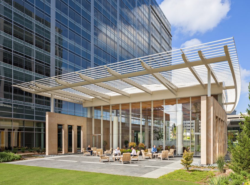 Cox Communications campus pavilion with a louvered canopy and outdoor seating beside the glass tower