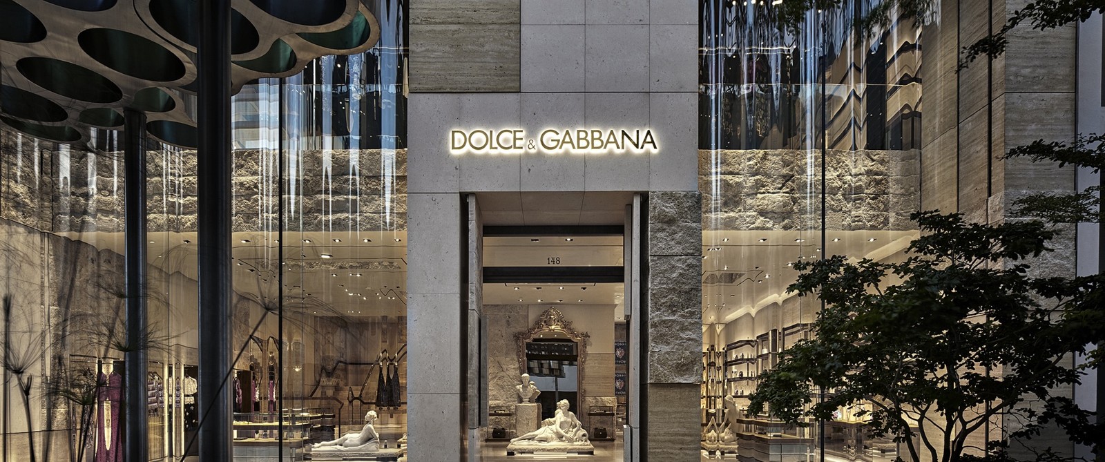 Dolce & Gabbana boutique entrance with illuminated sign, stone facade and glass storefront
