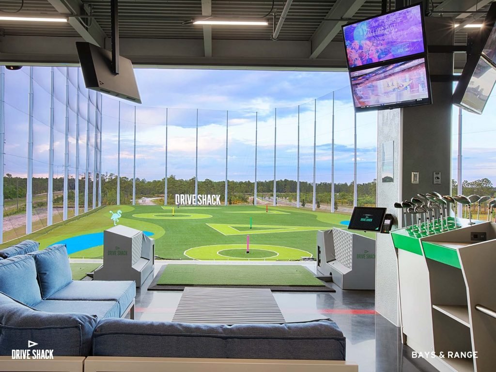 Drive Shack hitting bay with lounge seating, TVs and a view of the outfield