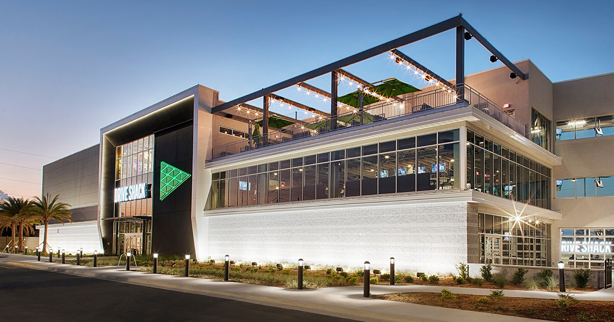 Drive Shack Lake Nona exterior at dusk with rooftop terrace and glowing green logo