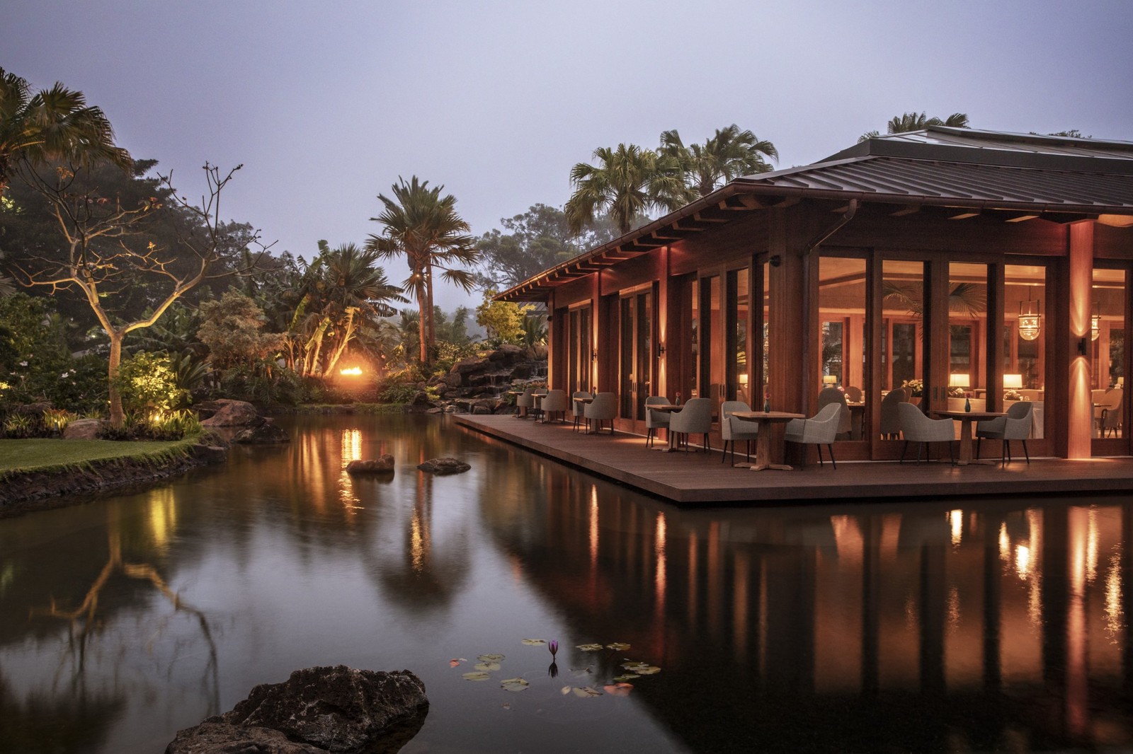 Four Seasons Lanai dining pavilion glowing at dusk beside a reflecting pond