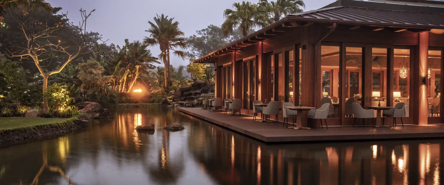 Hospitality dining pavilion at dusk with warm lighting reflected in a pond