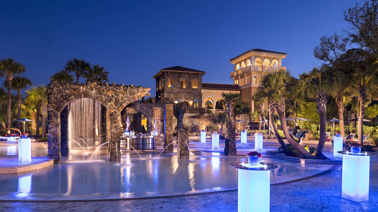 Four Seasons Walt Disney World pool area with stone arches and illuminated tables at night