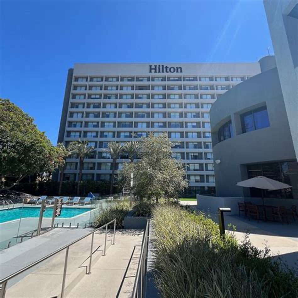 Hilton Culver City guestroom tower rising above the pool deck and landscaped courtyard