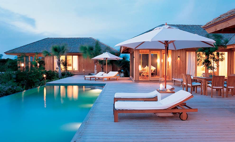 Poolside deck and villa glowing at dusk at Hotel Como Parrot Cay