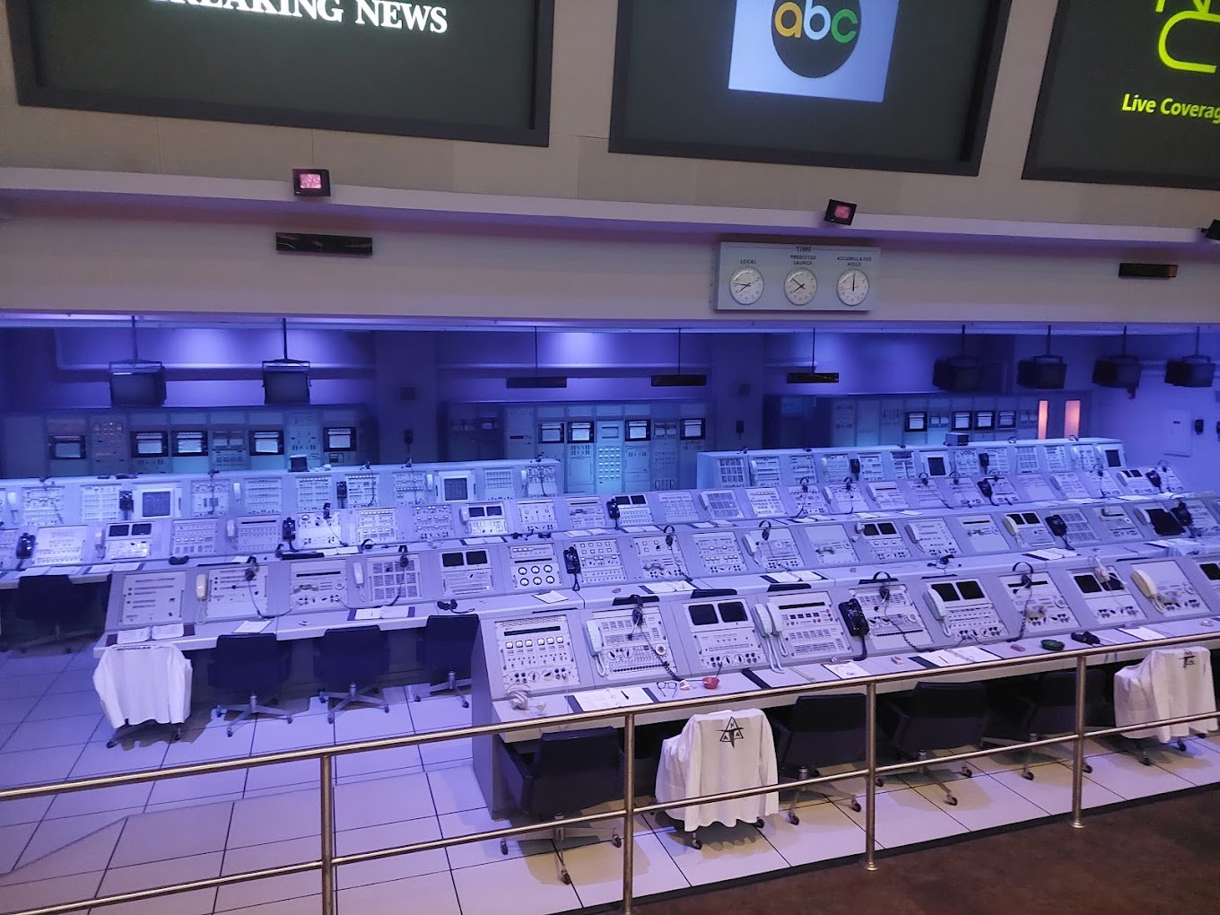 Historic launch control room at Kennedy Space Center with rows of consoles under blue lighting