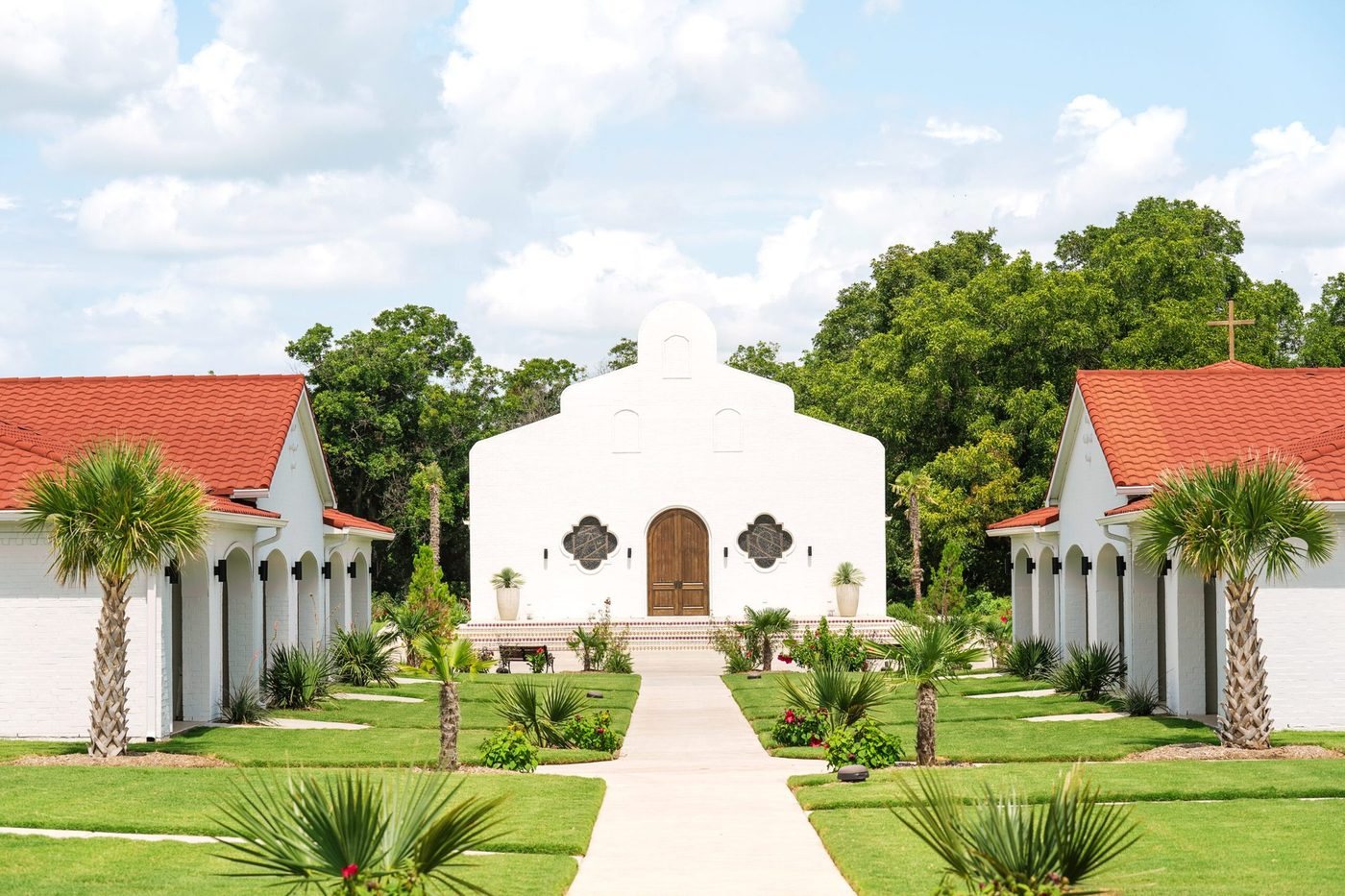 La Palmilla chapel with arched wooden doors, palms and red-tile casitas on both sides in Glen Rose, Texas