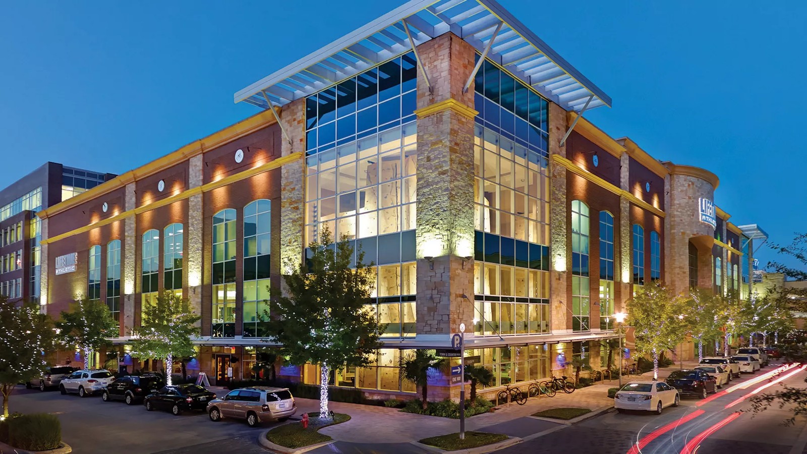 Lifetime Athletic building at dusk with glass corner, stone columns and lit trees