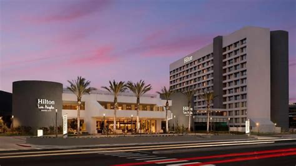 Hilton Culver City hotel exterior at dusk with palm trees, a glass entrance and a guestroom tower